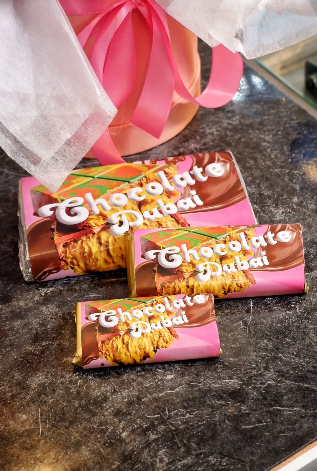 Tiga ukuran Chocolate Dubai Itacakeshop berbungkus pink di samping kotak berpita